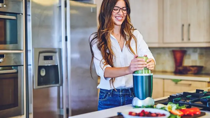 Woman in jeans and a white shirt making a calcium-rich green smoothie with low FODMAP vegetables