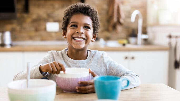 Happy, smiling boy eat a bowl of cereal at the kitchen table