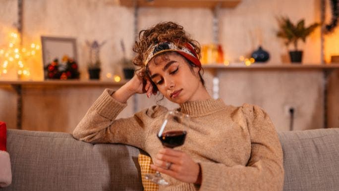 A young woman is sitting on a sofa and looking at a glass of red wine