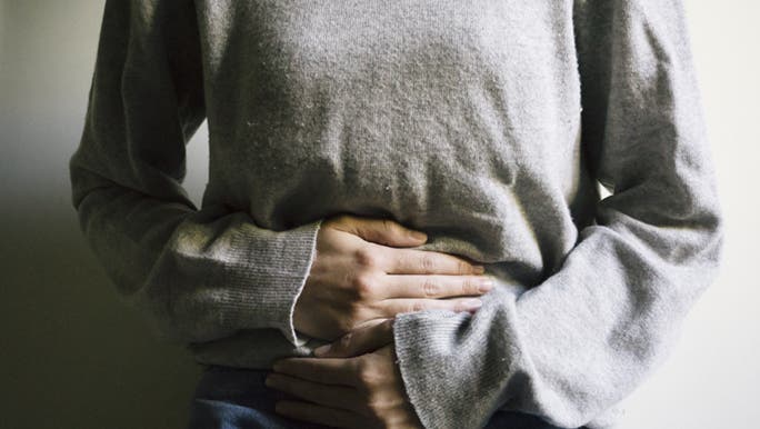 A close up shot of a woman holding her stomach, she is experiencing lower back period related pain. 
