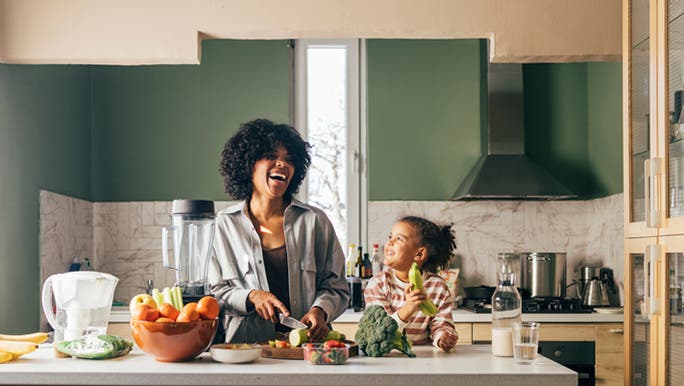 A woman of colour is laughing while chopping some of the best fruit for gut health with a young girl