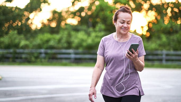 woman walking in the park listening to music and looking at her phone