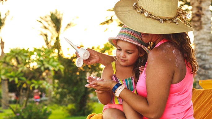 Mother teaching her little daughter how to use the sunscreen