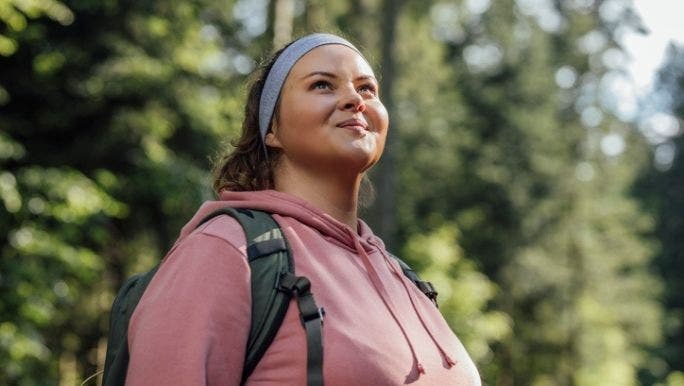 A young woman is walking in a forest and smiling as she admires her surroundings