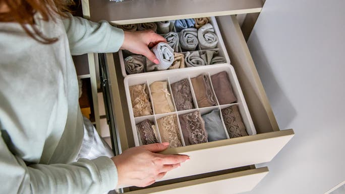 A woman is organising her clothes in a drawer filled with drawer dividers