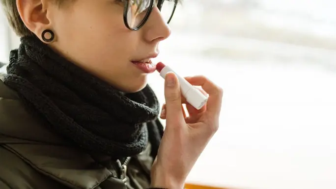 Woman with short blonde hair and glasses applying lip balm
