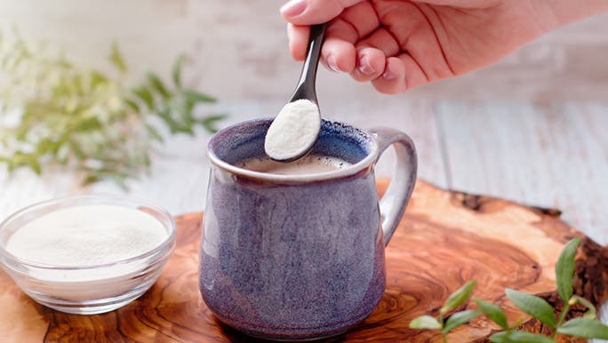 A woman spoons collagen protein powder into her coffee, as a prebiotic for gut health.
