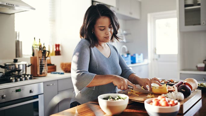 Woman in kitchen preparing vegetables for healthy hair and nails.