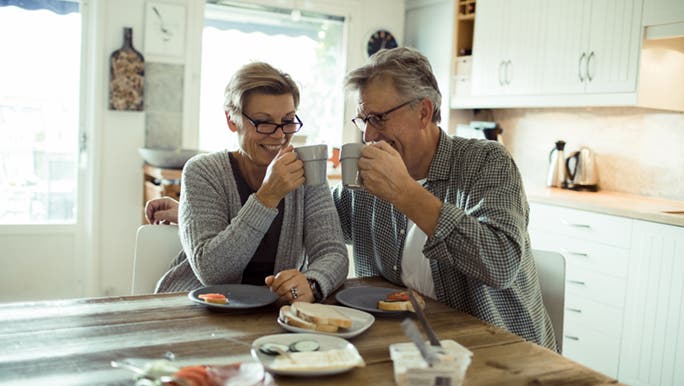 A middle aged couple sit at their wooden dining table drinking coffee as they discuss if they can drink coffee with probiotics.