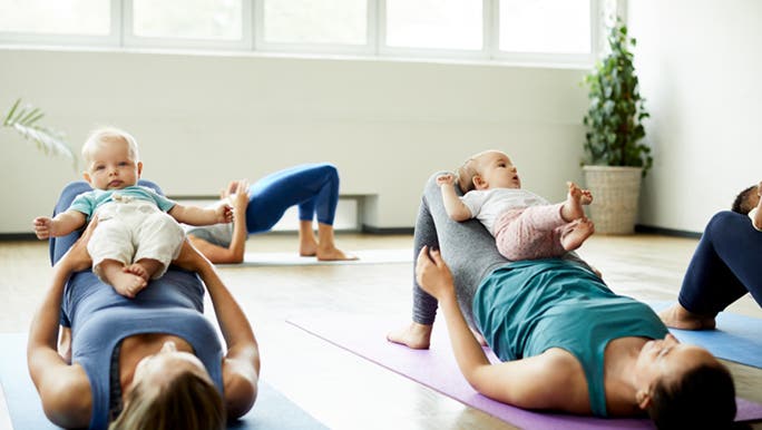 Two mothers are doing a mum and bub exercise class, they are laying down on their backs using their babies as weights.