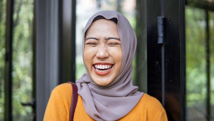 Happy young woman in a hijab and yellow cardigan laughing