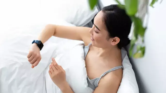 Young woman waking refreshed in the morning and checking her sleep tracker on her smartwatch