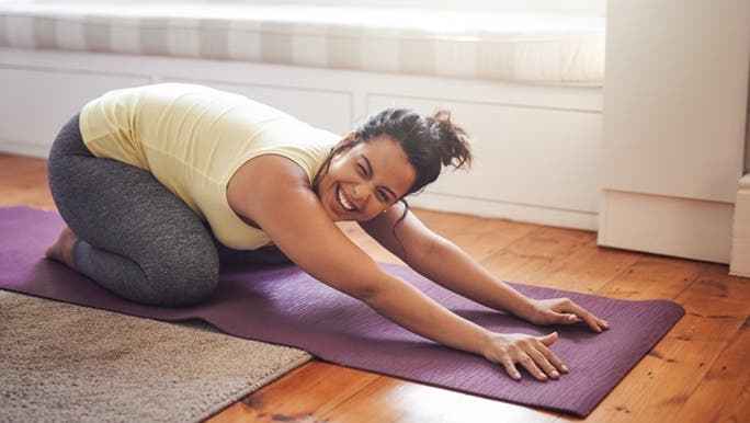 While on her yoga mat stretching out, a woman is smiling and happy because she is doing a free online yoga class.