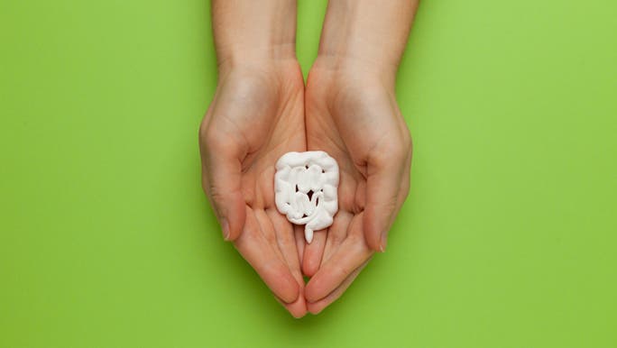 On a green background, two hands cradle a model of the intestine to explain gut dysbiosis.