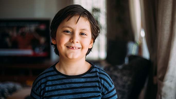 School aged child smiles at the camera with some baby teeth missing and thinks about if baby teeth can be crooked.