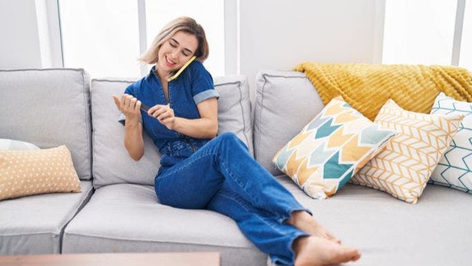 A young woman is relaxing on a sofa and filing her nails