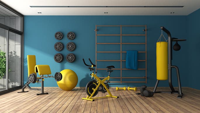 Colourful gym equipment sits in front of a blue wall as part of a home gym setup.