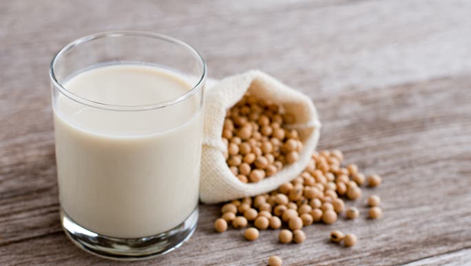 A glass of vegan soy milk sits next to a bag of soybeans. 