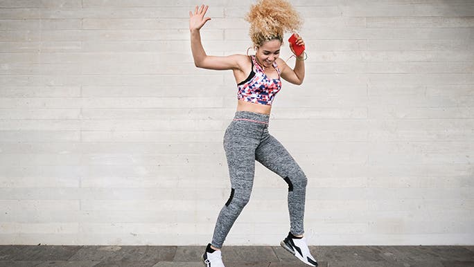 A woman in exercise clothes is dancing to some music through headphones and might be wondering if exercise helps the immune system. 