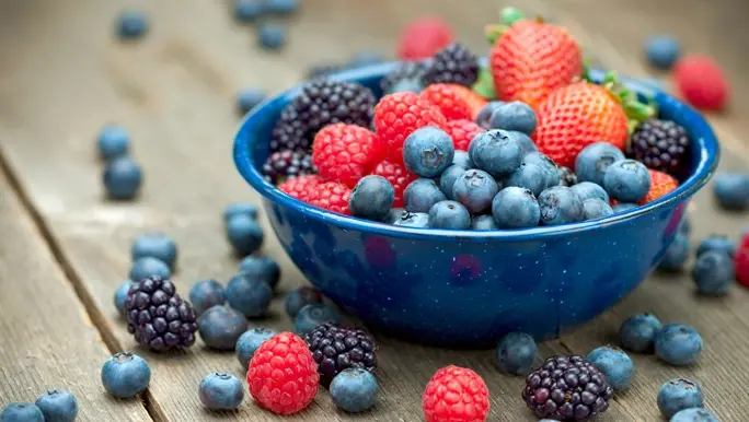 Low FODMAP raspberries, blueberries and blackberries in a blue bowl on a timber surface