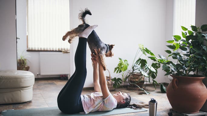A woman is laying on her back in her apartment on a yoga mat, she is lifting her god with her feet and stretching after a long run. 