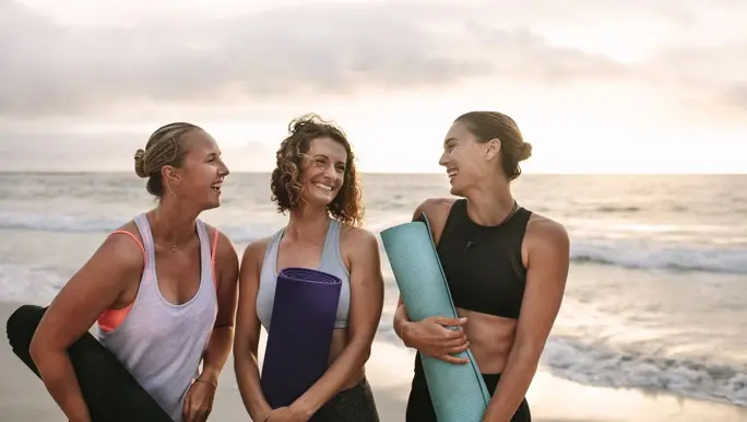 Three female friends on the beach with yoga mats