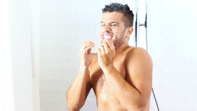 A young Caucasian man is taking a cold shower and flinching at the temperature