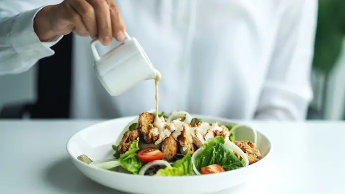 Man in white shirt pouring dressing on a low FODMAP salad