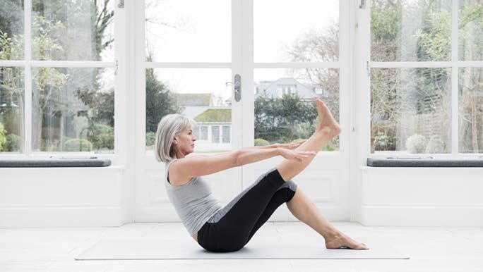 A woman with grey hair stretches on a yoga mat after reading about how to get flexible fast.