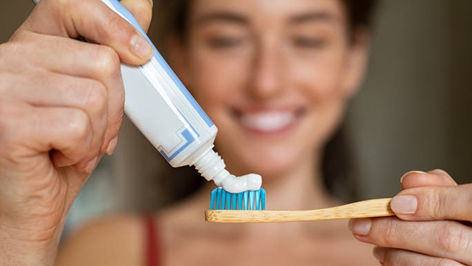 Squeezing toothpaste onto her toothbrush, a woman smiles after learning how long to brush her teeth for. 