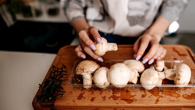 Woman preparing mushrooms on a wooden chopping board