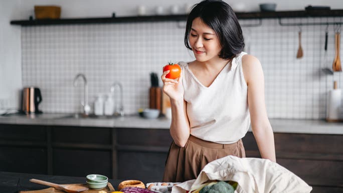 A woman smiles while looking down at the fresh produce she bought as making healthier changes in her diet is relevant to gut health and anxiety.  