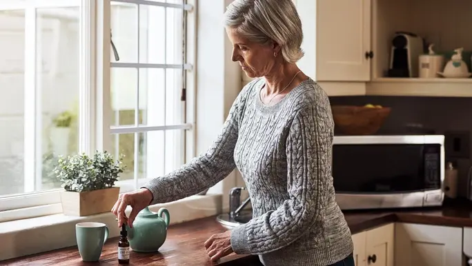 Woman at home in the kitchen adding CBD oil to her tea