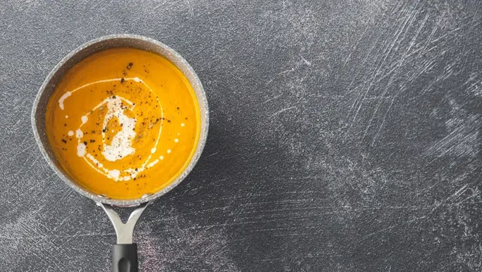 Carrot and ginger soup in a saucepan on a dark grey benchtop