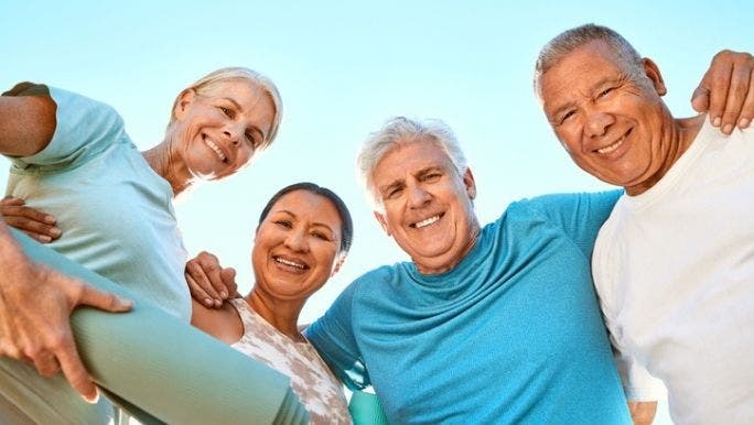  A group of senior people are standing in a circle wearing activewear and looking into the camera smiling
