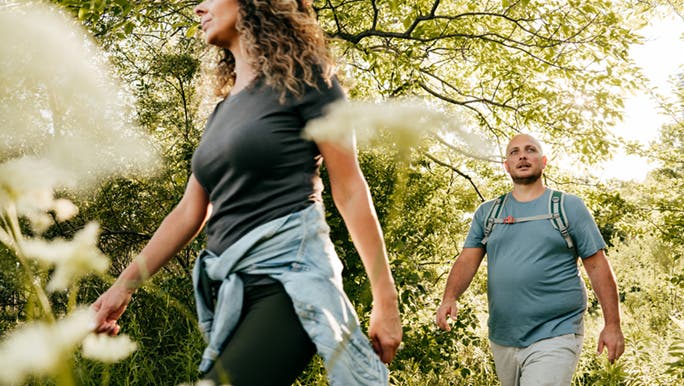 A man and woman walk through the bush, they are prioritising fitness as they age healthily. 