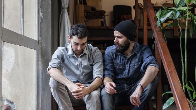 Two young men sitting on a stairway having a serious conversation about men’s mental health
