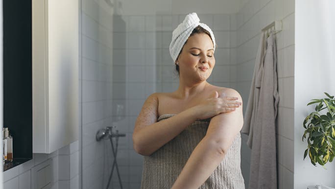 A lady dressed in a towel is applying moisturiser after her shower. Hopefully she is exploring how to boost her self worth. 