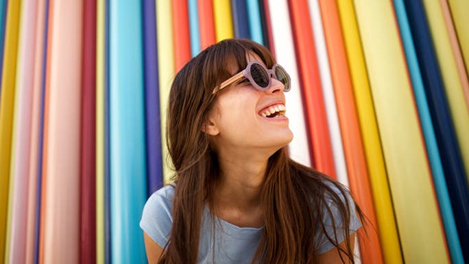 A woman smiles in front of a colourful background. She is outside decluttering her mind during her lunch break. 
