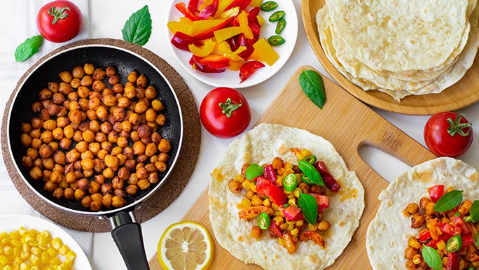 A table full of vegan food, lemons, tomatoes basil and wraps etc. 