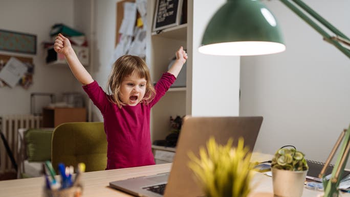 A little girl celebrates with her hands in the air. She is looking at a laptop and appears to have nailed some productivity hacks. 