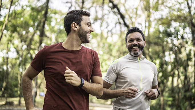 Two men are outside smiling while running and one of them is wearing a cheap fitness watch. 