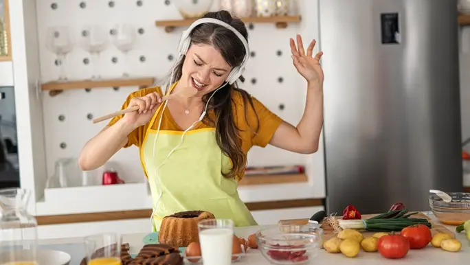 Young woman dressed in yellow and listening to music through headphones having fun in the kitchen
