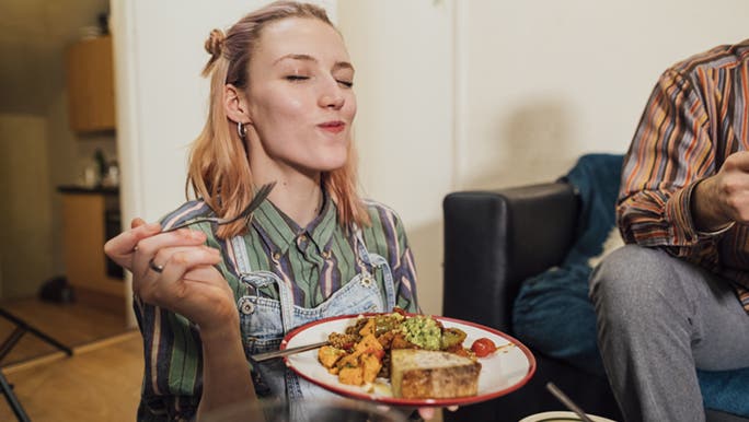 A woman smiles while eating a vegan meal with her friends as she already knows how to go vegan.