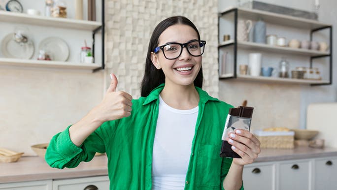 A young woman with long dark hair and wearing a green shirt is eating dark chocolate, which is part of the low FODMAP food list