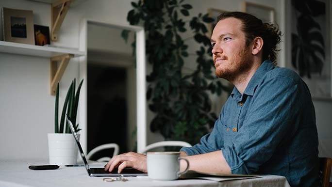 Man sits at his desk in front of his computer thinking about work related stress.
