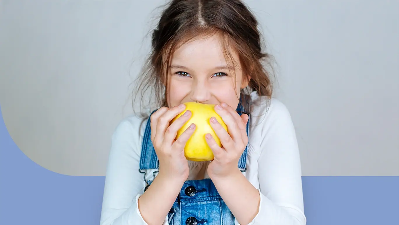girl in overalls eating a yellow fruit