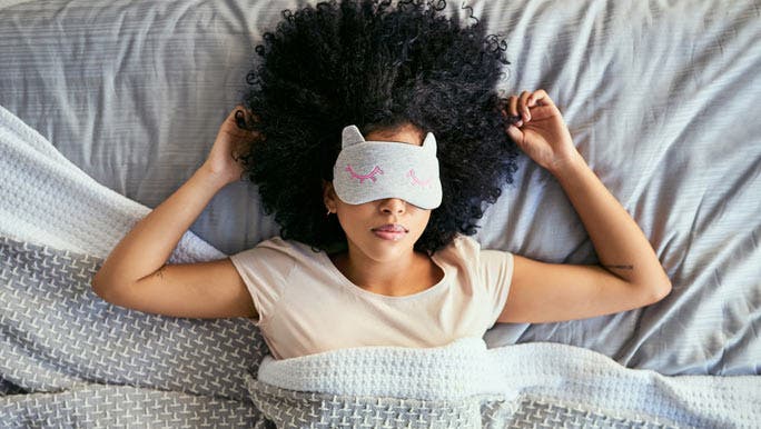 Young woman sleeping peacefully in bed and wearing a cute animal shaped eye mask