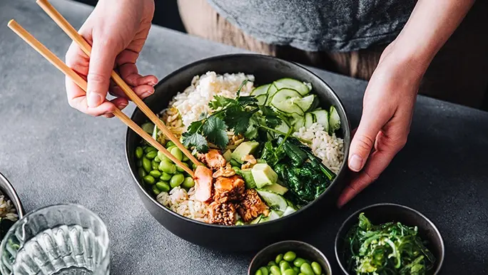 Person holds salad bowl filled with fresh ingredients including grains, which are a good source of resistant starch to help support gut health.
