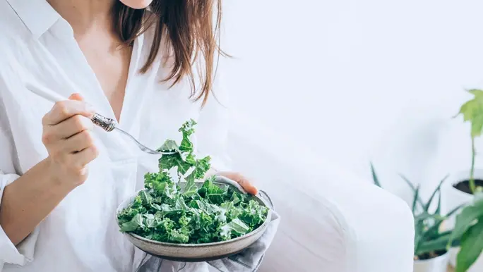 Woman in a white shirt eating a kale salad